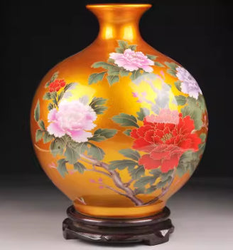 Golden ceramic vase with pink and red peonies, green leaves, glossy base.