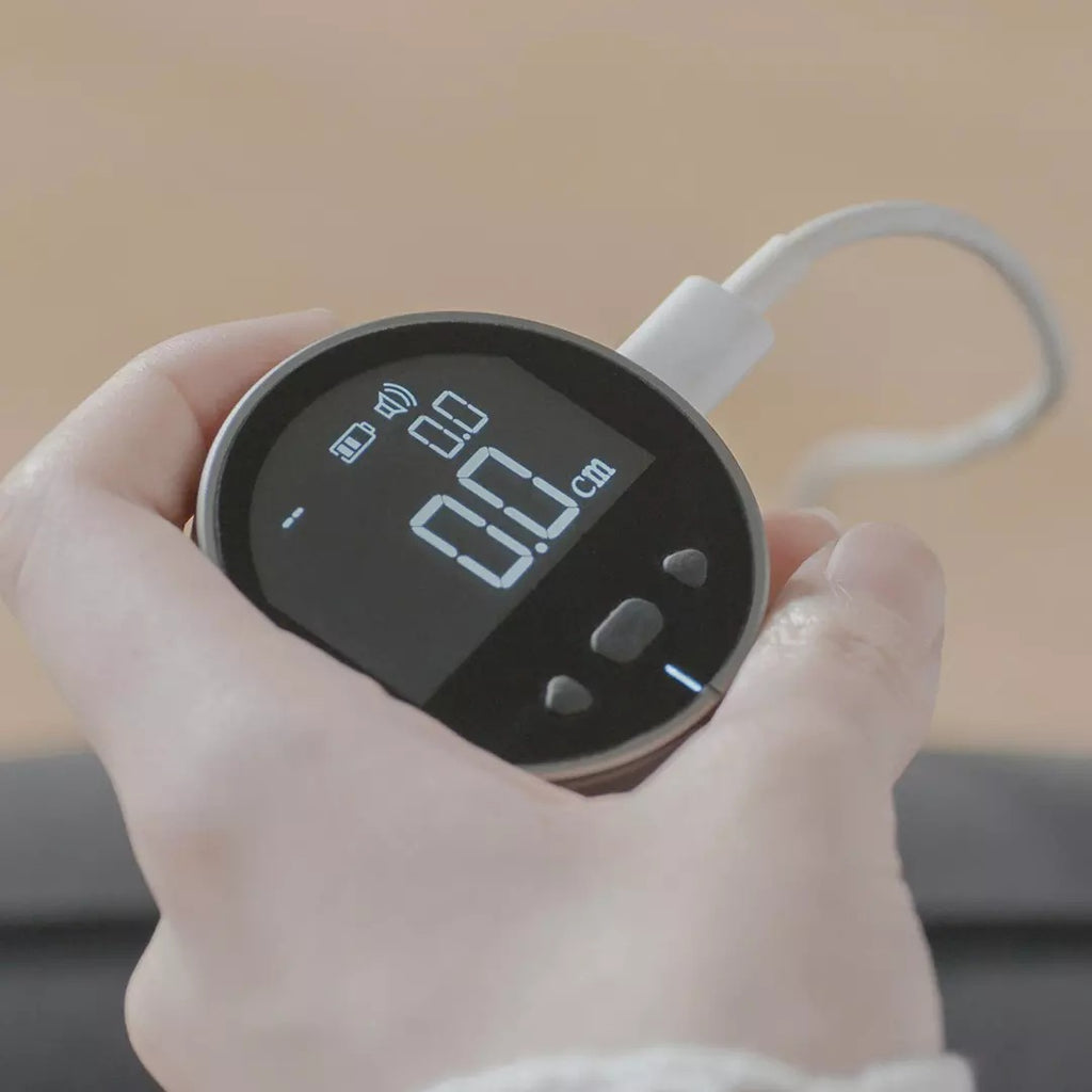 Handheld electronic measuring ruler with round black LCD displaying a distance in cm