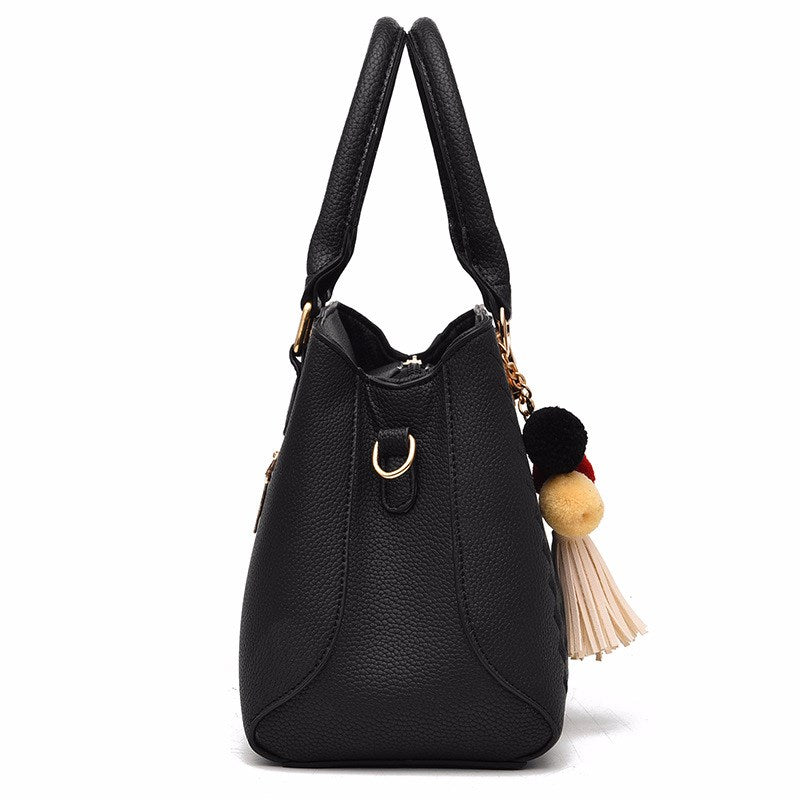 Black textured handbag with shoulder handles, crossbody strap, and tassel pom charm