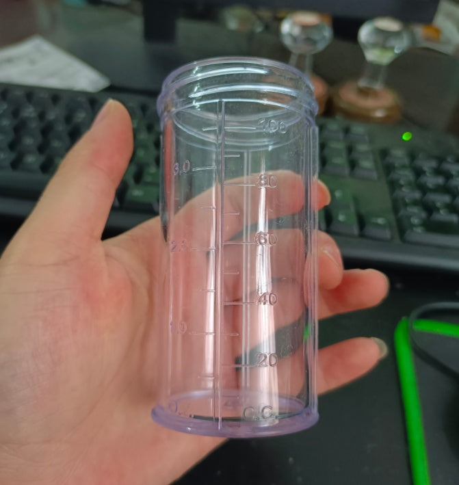 Clear measuring cup for foam spray gun with scale markings, held in a hand